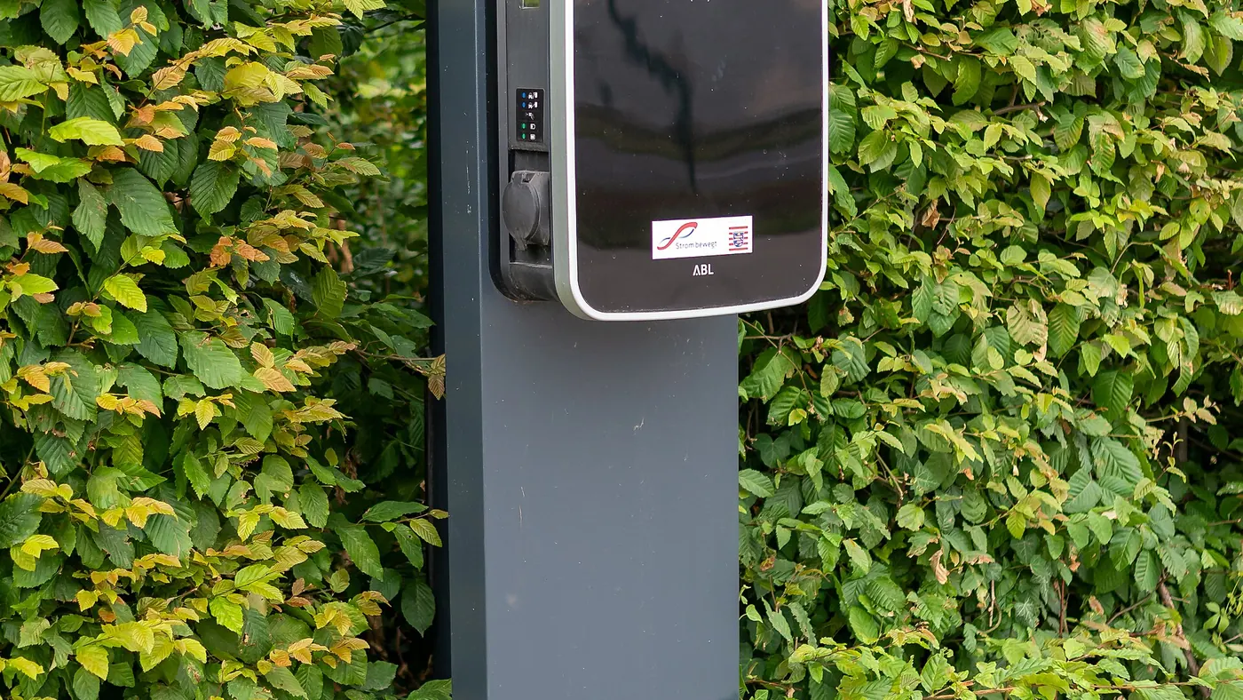 Borne de recharge murale installée contre un mur extérieur, le long d'une haie